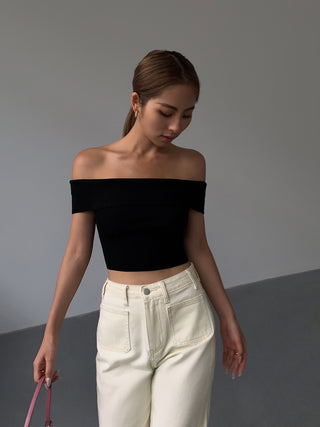 Stylish off-the-shoulder black knitted crop top, paired with high-waisted white trousers, showcasing a modern, minimalist fashion look.
