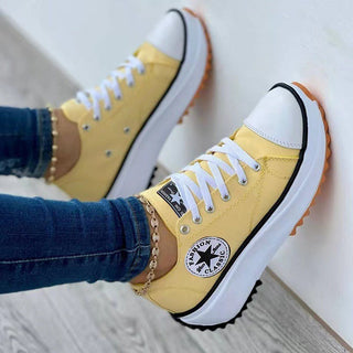 Trendy yellow canvas sneakers with white soles and black laces. The sneakers feature the iconic Converse All-Star logo and appear to have a platform or thick sole design. The sneakers are shown on a person's feet, worn with jeans.