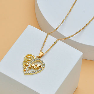 Elegant gold heart-shaped necklace with the word "Mom" and diamond accents, showcased on a white pedestal against a neutral background.