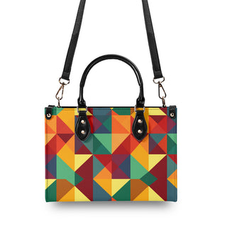 Colorful geometric patterned tote bag with black leather handles and detachable shoulder strap from K-AROLE. The handbag features a vibrant array of triangular shapes in warm hues of orange, yellow, and green.