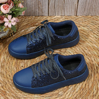 Glittery navy blue sneakers with lace-up closure, showcased on a woven mat backdrop with floral decorations.