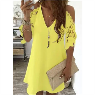 Vibrant yellow dress with lace details, worn by a woman with long brown hair, accessorized with jewelry and a beige handbag.