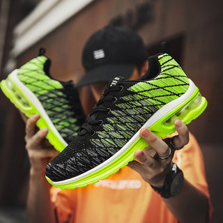Stylish neon green and black sneakers with air cushion soles, worn by a person in casual attire holding the shoes in their hands.