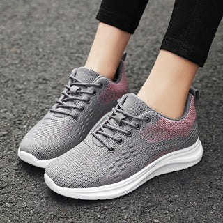 Lightweight breathable women's sneakers with pink and grey mesh upper, lace-up design, and white sole on a paved ground.
