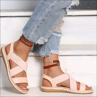 Stylish summer sandals with criss-cross straps and a flat, comfortable sole displayed against a backdrop of distressed denim jeans.