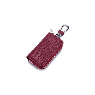 Compact leather key holder in burgundy with crocodile texture, featuring a zipper closure and metal clasp for convenient key storage and organization.