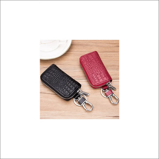 Premium leather key holder in black and red. Compact wallet-style pouch with zipper closure to securely organize and carry car keys, key fobs, or other small items. Stylish and practical accessory for everyday use.