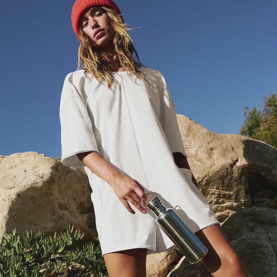 Stylish white dress with long sleeves, fashionable red beanie, and metal water bottle in the outdoor natural setting.