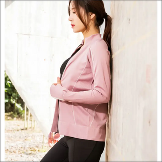 Stylish slim-fit pink sportswear, featuring a tailored design and long sleeves, worn by a young woman standing near a white wall.