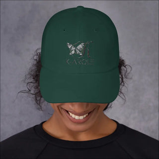 Stylish green dad hat with K-AROLE logo and butterfly design, worn by a smiling person against a gray background.