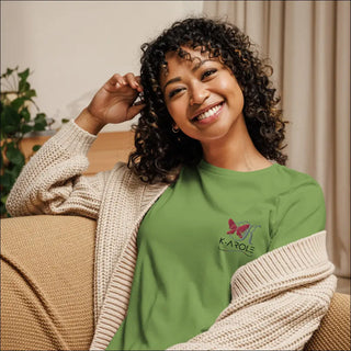 Smiling woman in green K-AROLE branded t-shirt and cozy neutral cardigan, seated against an interior background.