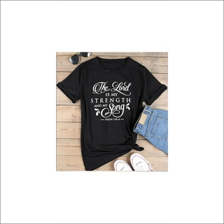 Stylish black t-shirt with inspirational Christian text "The Lord is my strength and song" displayed on wooden backdrop with casual accessories.